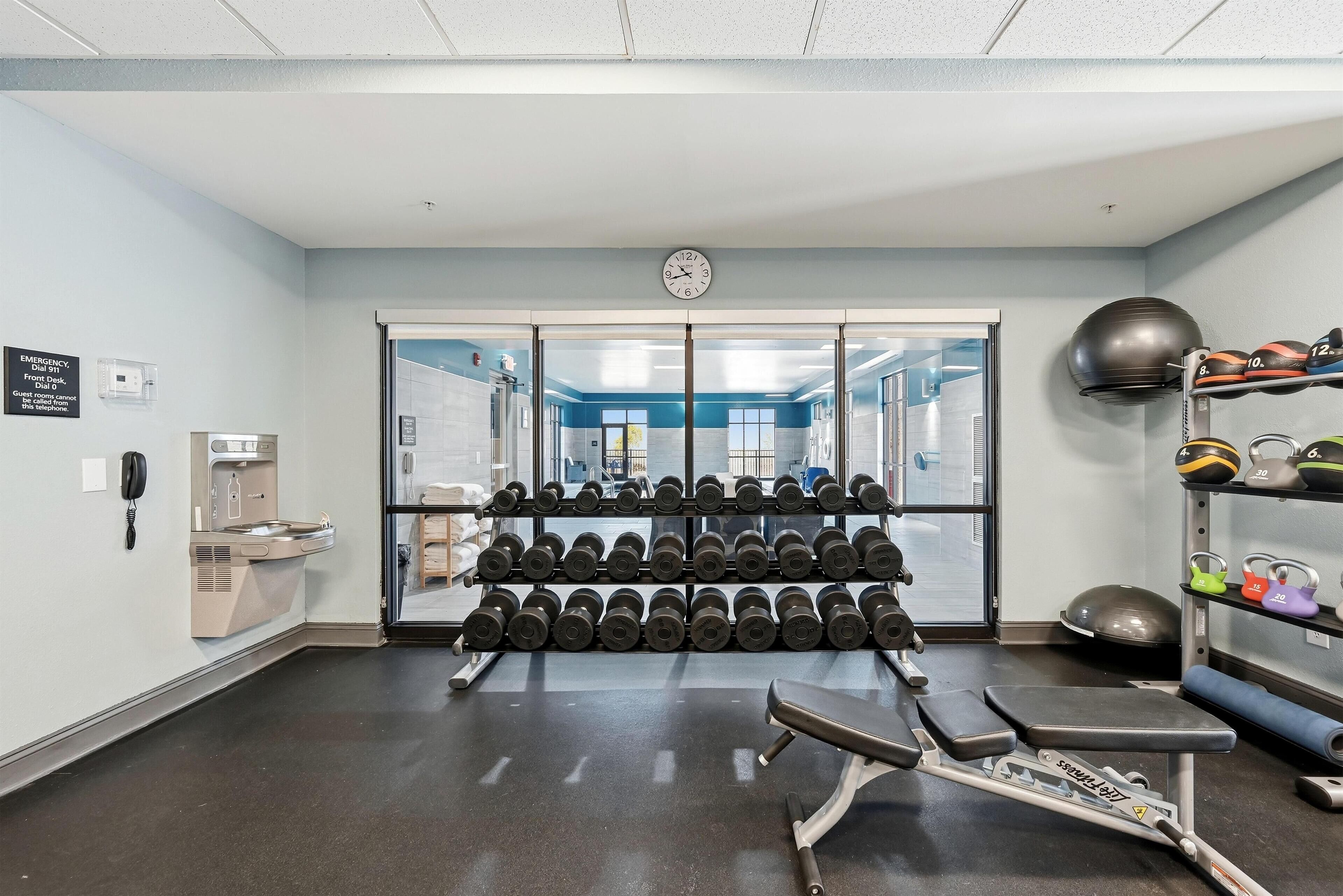 A gym with weight racks, a bench press, and a wall clock.