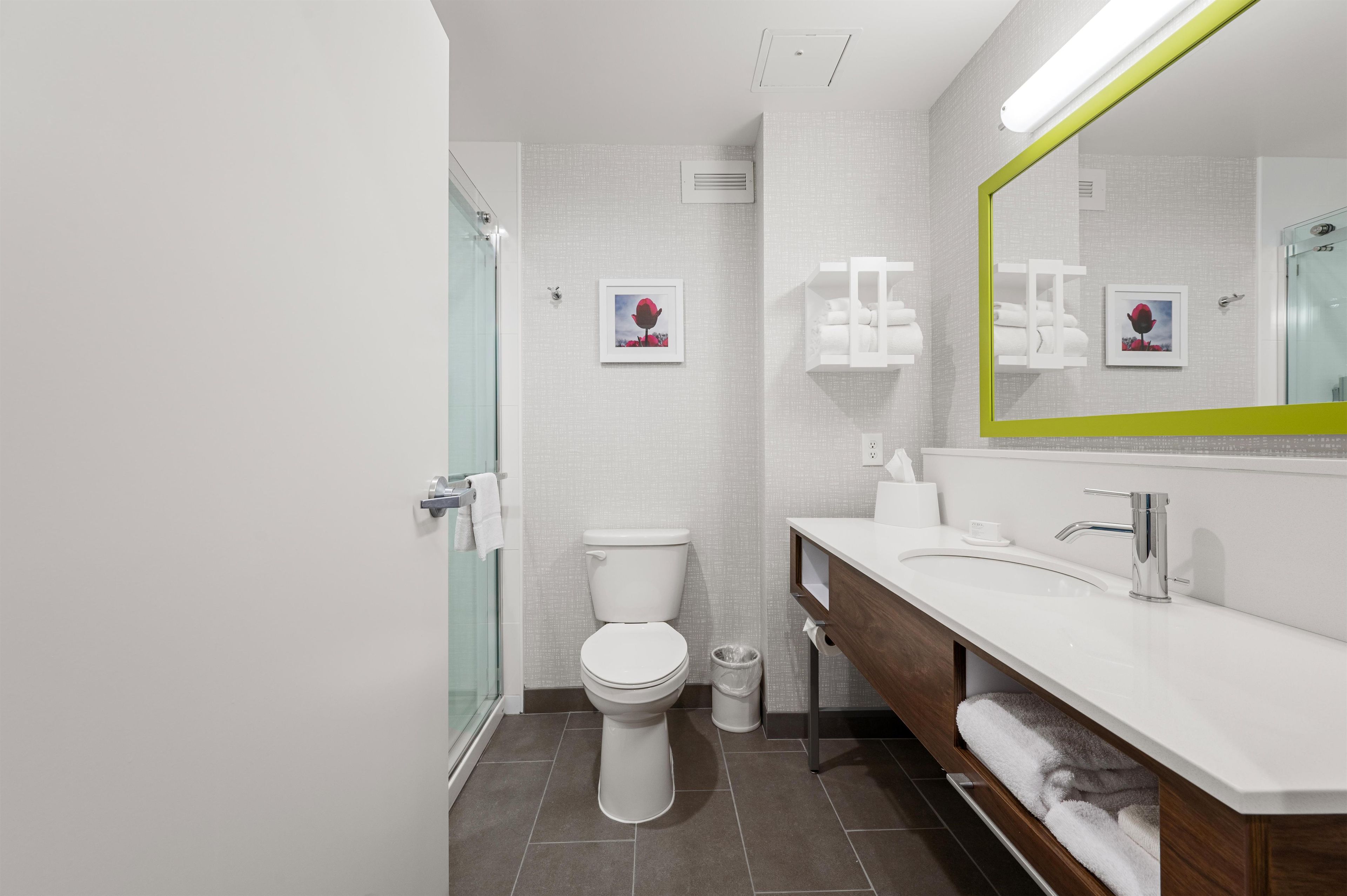 A modern bathroom with a glass shower enclosure, a toilet, a vanity with a mirror, and a towel rack.