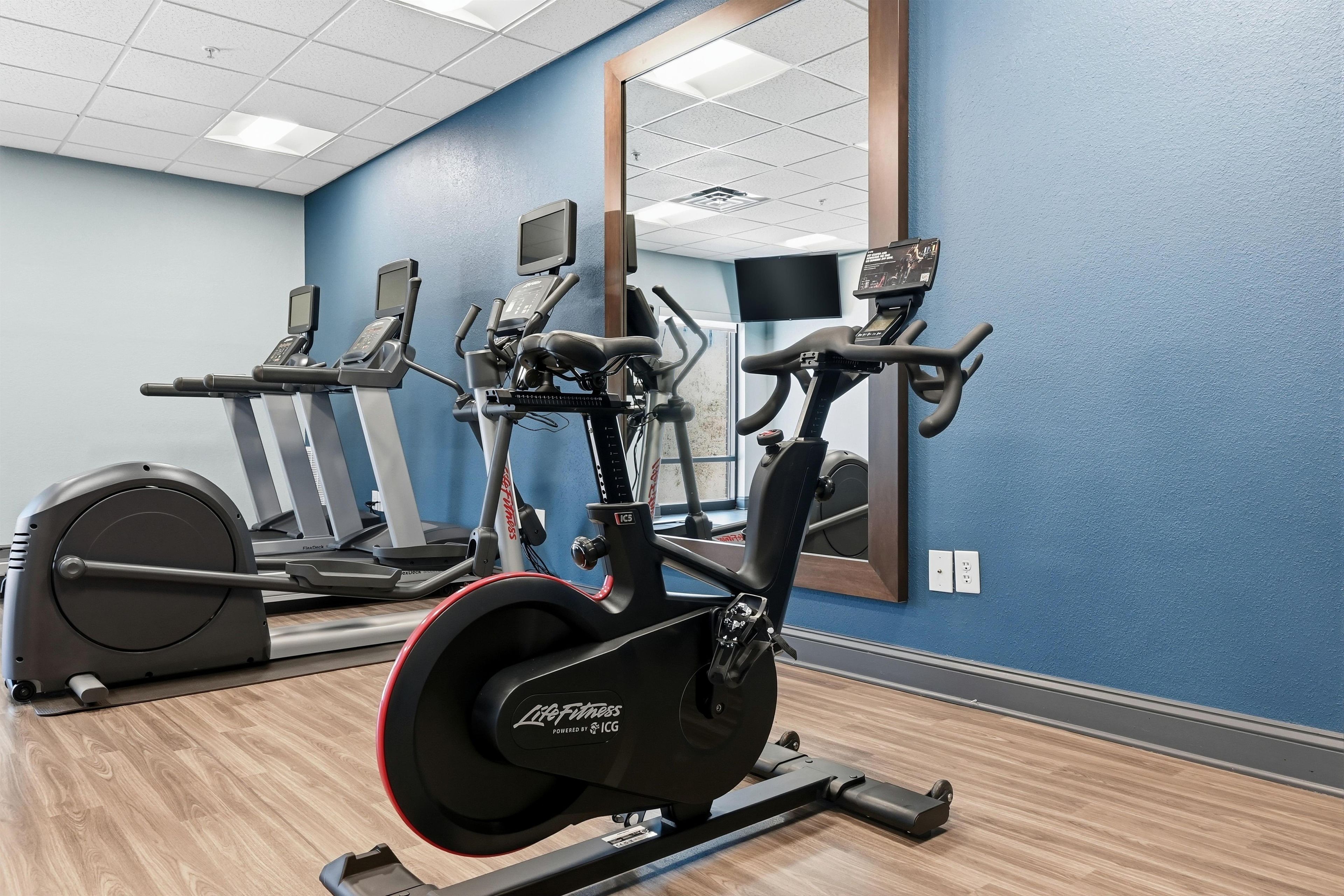 Une salle de sport équipée de vélos d’appartement, d’un tapis de course et d’un rameur.