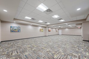 Une grande salle de conférence dotée d’un tapis à motifs, de luminaires encastrés au plafond et d’œuvres d’art accrochées aux murs.