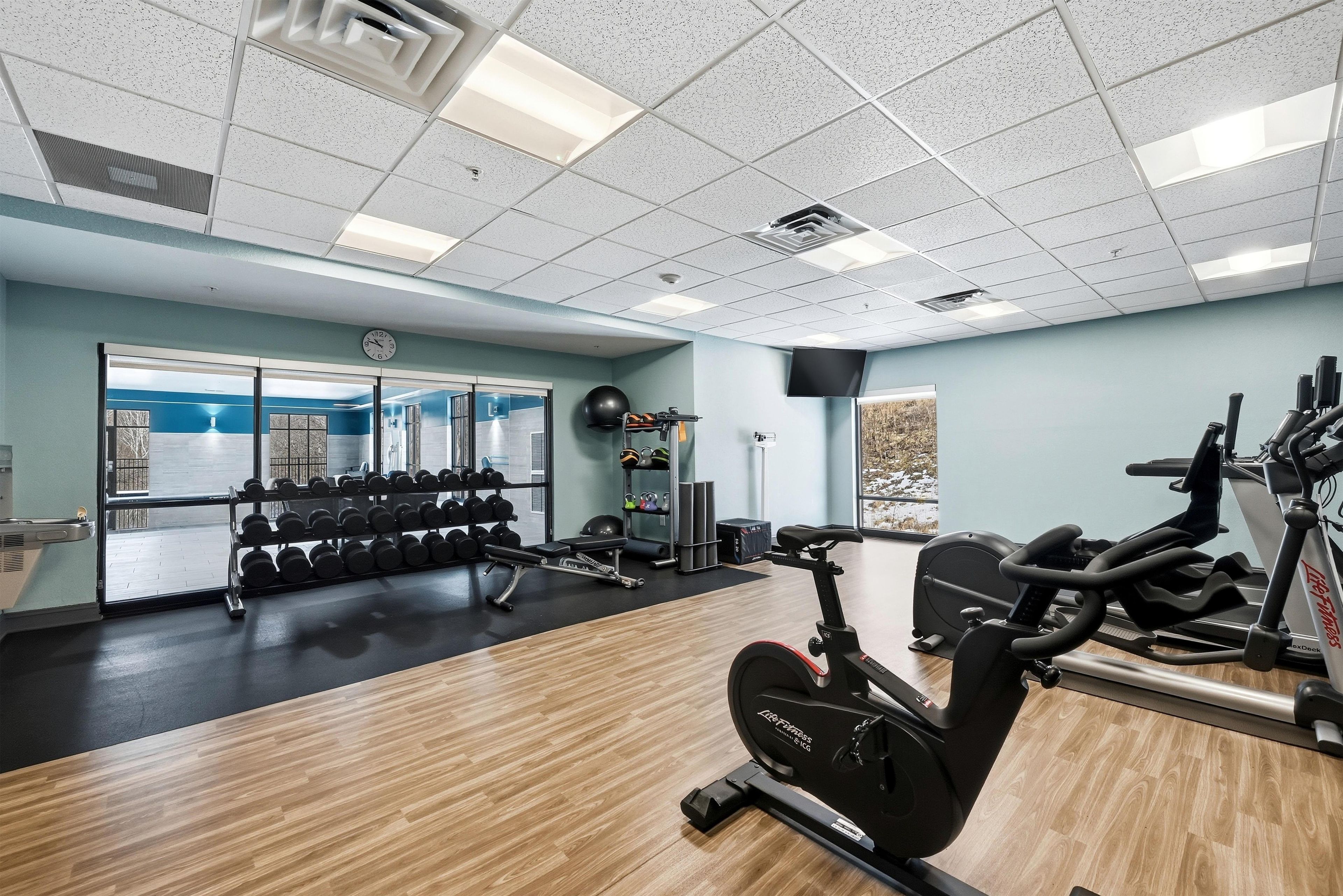Une salle de sport équipée de matériel d’exercice, d’un miroir et d’une fenêtre donnant sur un paysage enneigé.