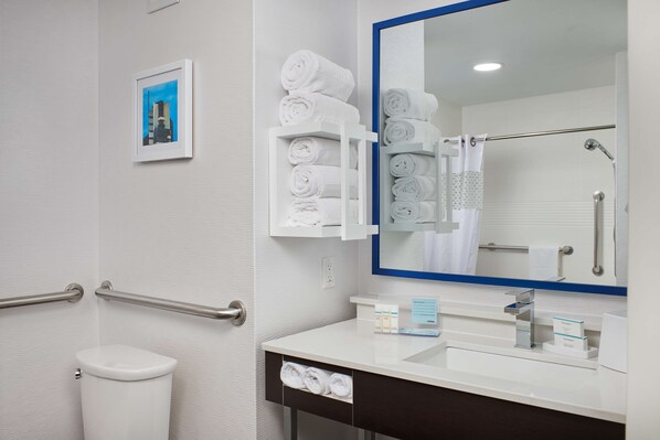 Un baño moderno con inodoro blanco, lavamanos con espejo y toallero con toallas dobladas ordenadamente.
