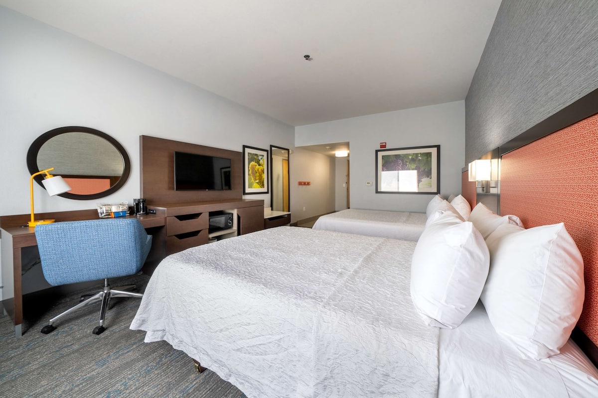 A hotel room with a bed, a desk, a chair, a TV, and a mirror.