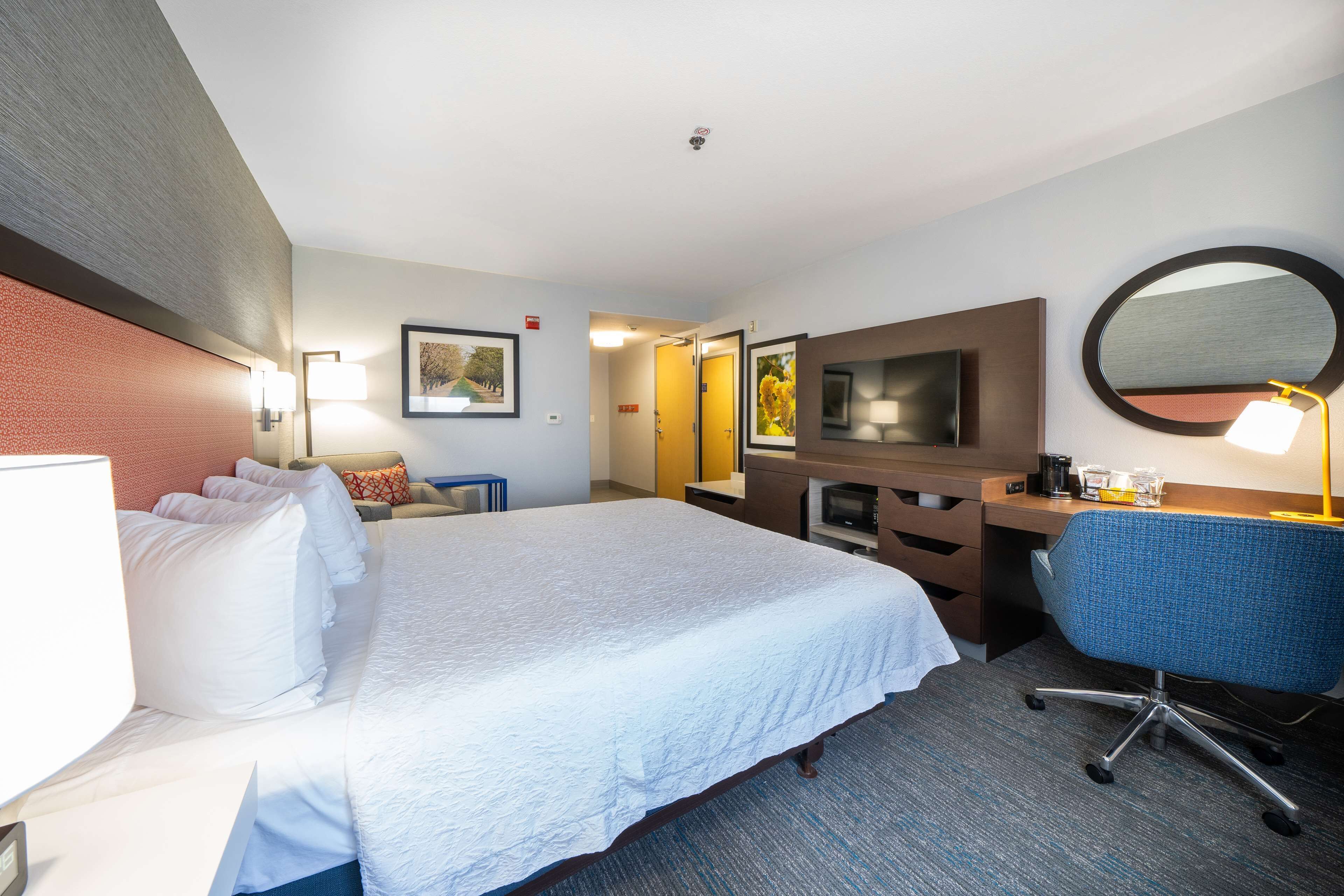A hotel room with a large bed, a desk with a chair, a flat-screen TV, and a mirror.