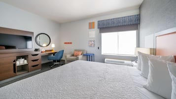 Habitación de hotel moderna con una cama grande, un escritorio con computadora, una silla y un televisor.