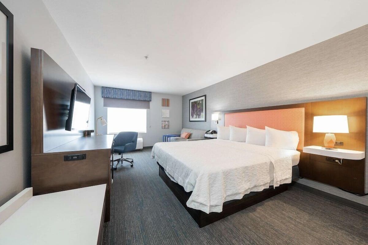 A hotel room with a bed, desk, chair, and a TV.