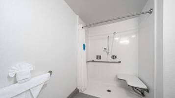 Un bagno moderno con cabina doccia in vetro, soffione a mano, sedile per doccia e porta asciugamani con un asciugamano piegato.