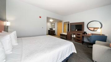 A hotel room with a large bed, a desk with a chair, a mirror, and a television.