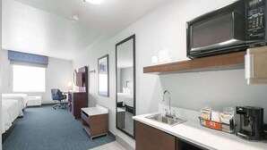 Quarto de hotel com cozinha compacta, uma cama, escrivaninha e uma cadeira.