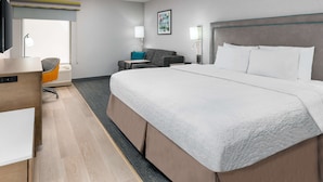 A hotel room with a large bed, a desk, a chair, and a sofa.