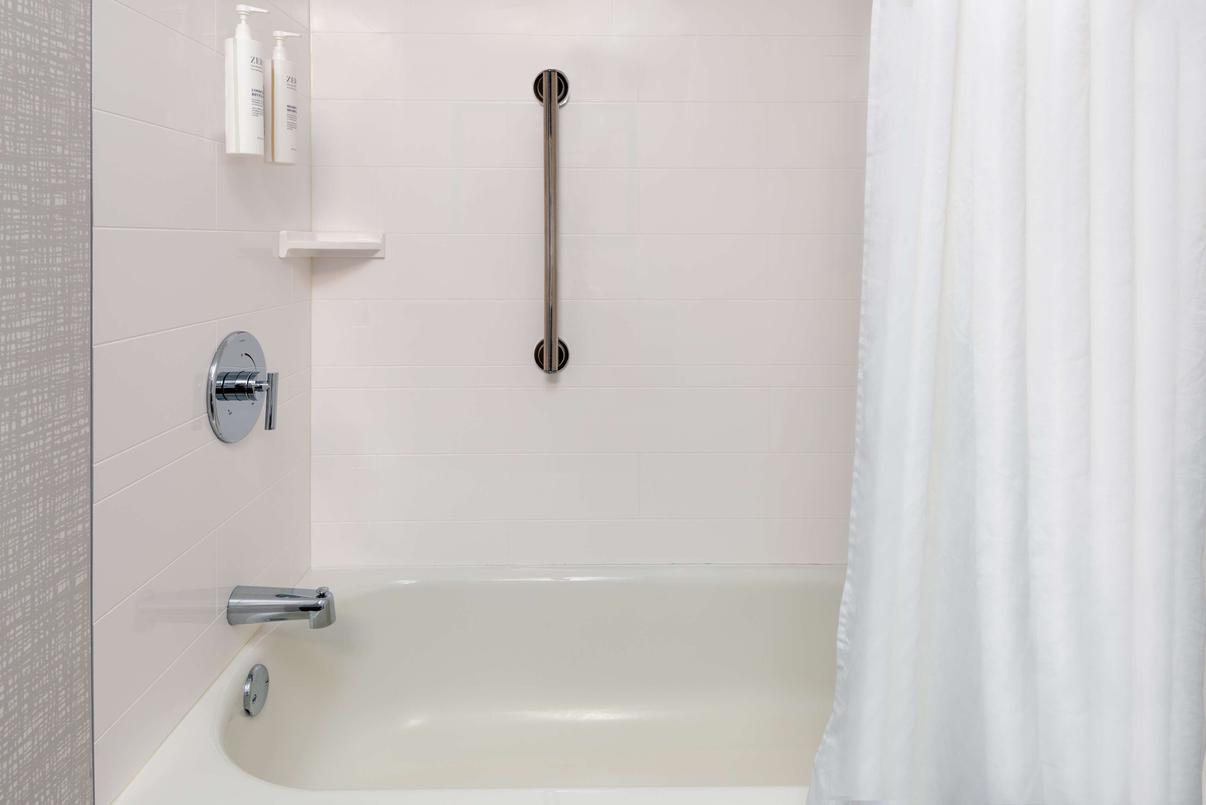 Une salle de bain moderne avec une baignoire, une barre d’appui et un rideau de douche.
