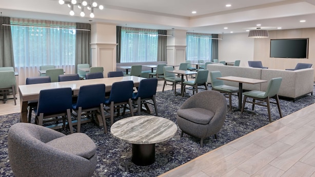 A modern hotel room with a dining area, seating arrangements, and a large TV screen.