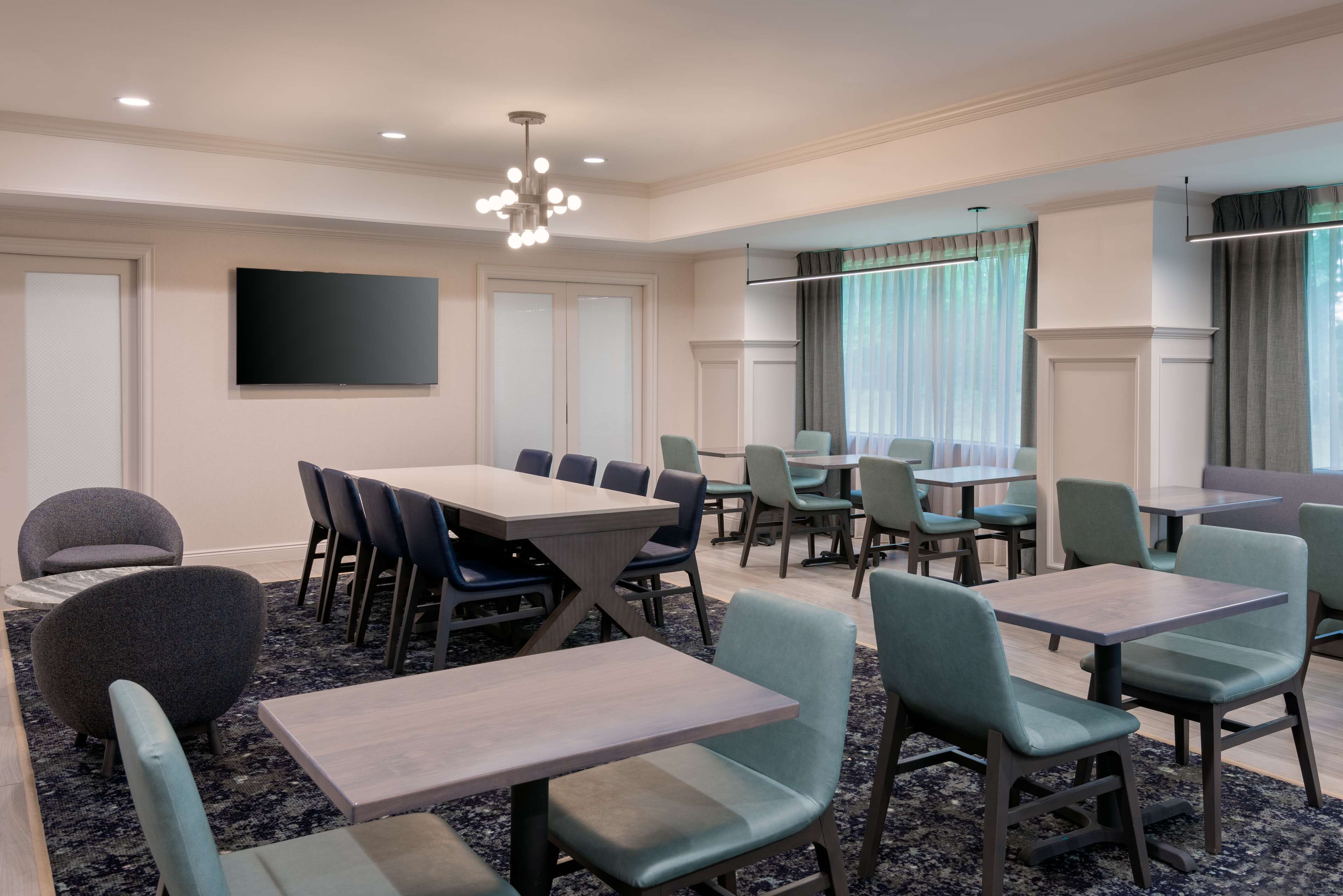 A conference room with multiple tables and chairs, a flat-screen TV, and a chandelier.