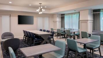 A conference room with multiple tables and chairs, a flat-screen TV, and a chandelier.