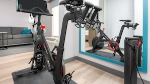 A modern living room with a grey sofa, a black exercise bike, and a large mirror reflecting the room.