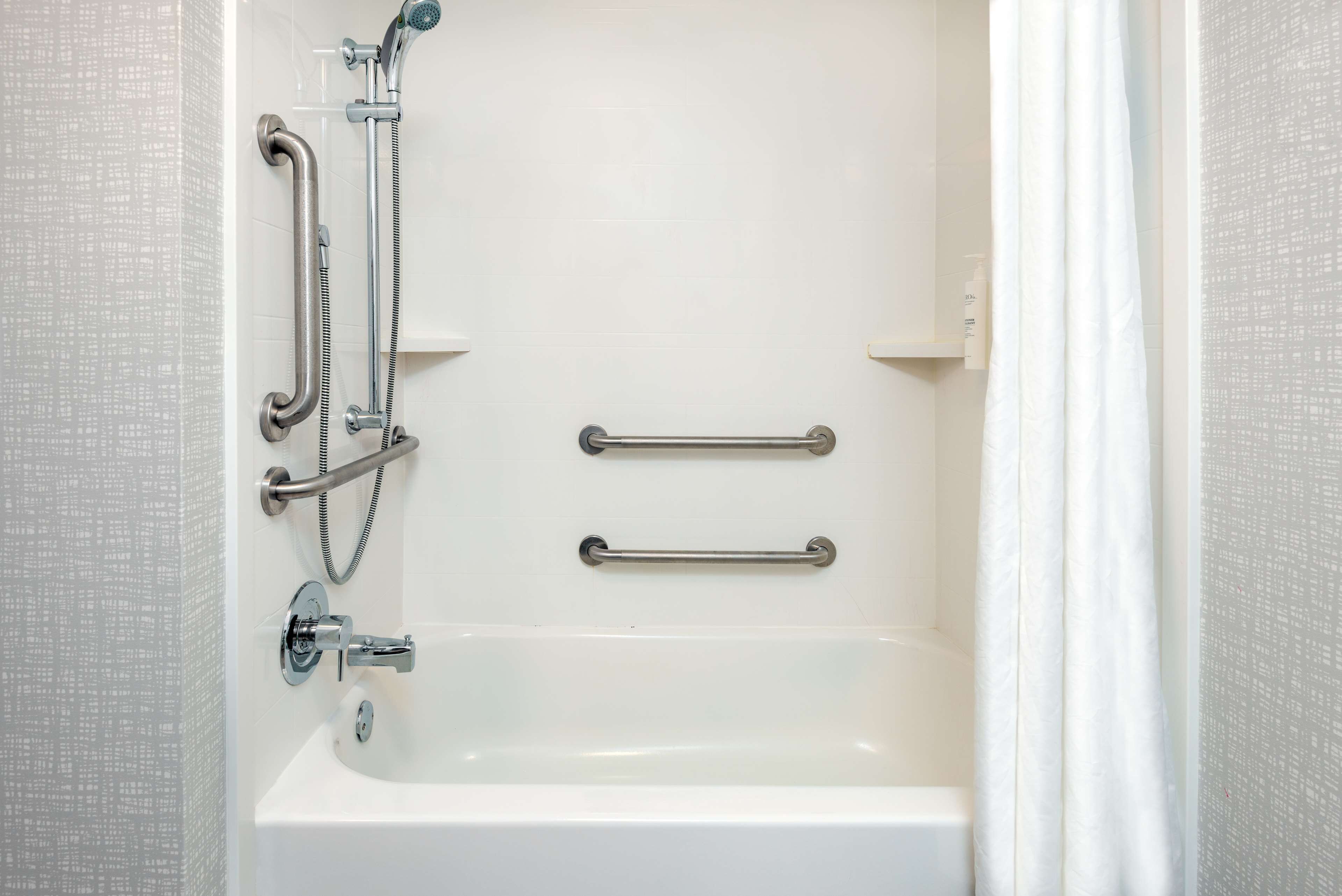 A white bathtub with a handheld showerhead and grab bars.