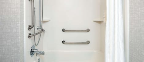 Una bañera blanca con cabezal de ducha de mano y barras de apoyo.