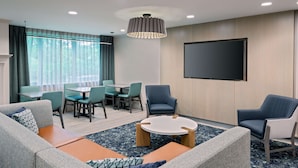 A modern hotel room with a seating area, a flat-screen TV, and a dining table.