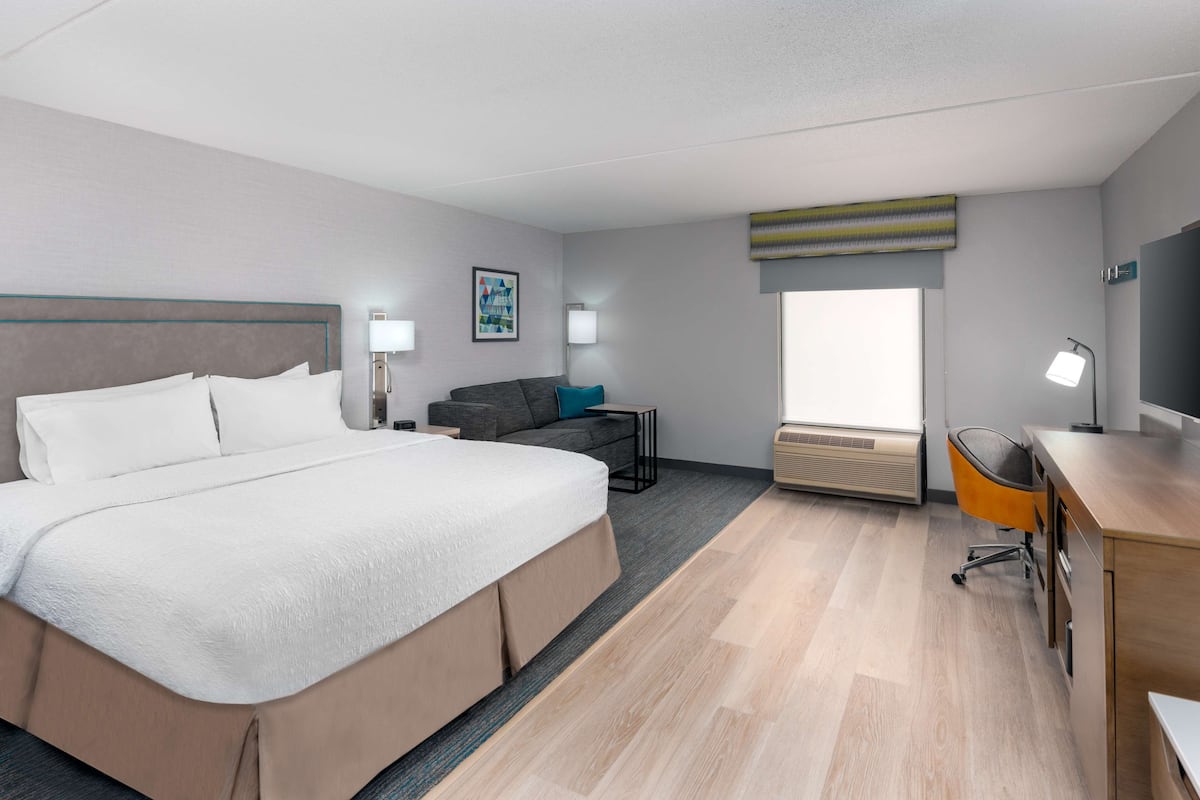 A modern hotel room with a large bed, a desk, a chair, and a window.