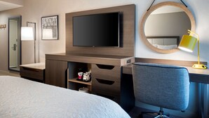A hotel room with a bed, a desk with a chair, a TV, a mirror, and a lamp. - Hampton Inn by Hilton Boston/Cambridge (Cambridge)