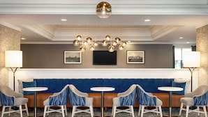 A seating area with a blue sofa, two round tables, and four chairs. - Hampton Inn by Hilton Boston/Cambridge (Cambridge)