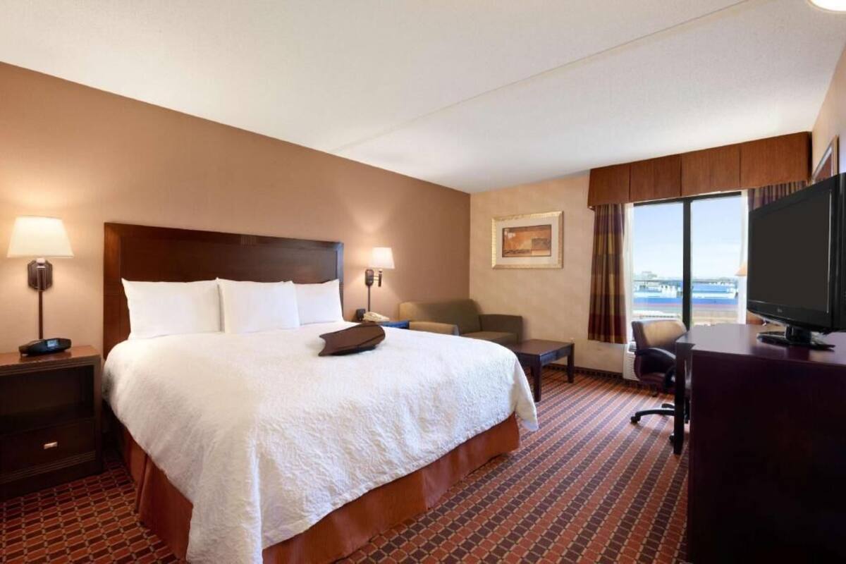 A hotel room with a large bed, a desk, a chair, a television, and a window with a view.