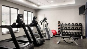 A gym with treadmills, an elliptical, a bench press, and a rack of dumbbells. - Hampton Inn by Hilton Boston/Cambridge (Cambridge)