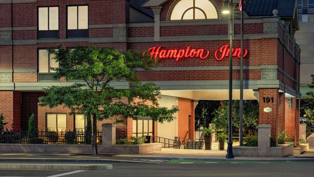A Hampton Inn hotel with a prominent red neon sign, brick facade, and a well-lit entrance. - Hampton Inn by Hilton Boston/Cambridge (Cambridge)