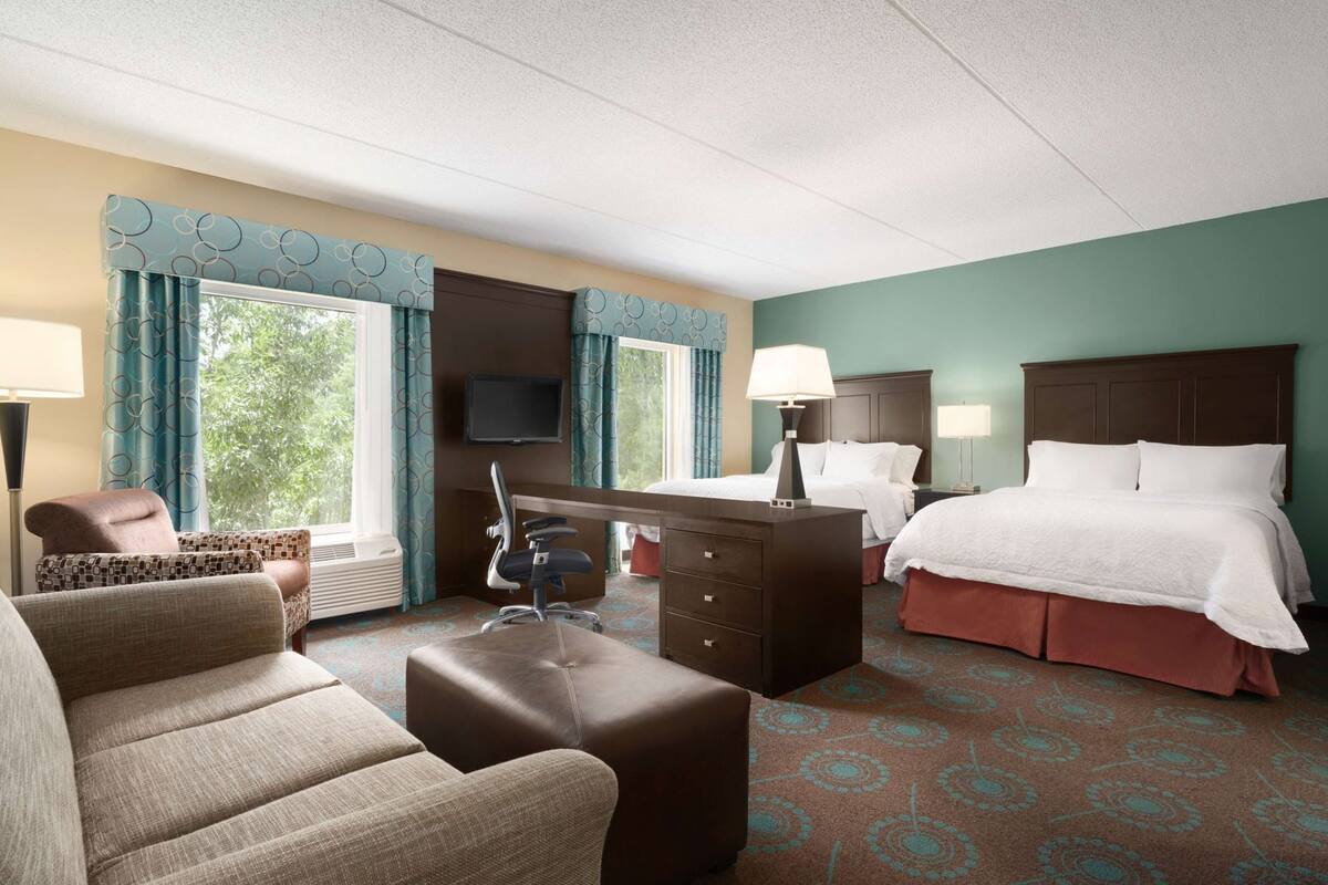 A hotel room with a bed, a desk, a chair, a TV, and a window with curtains.