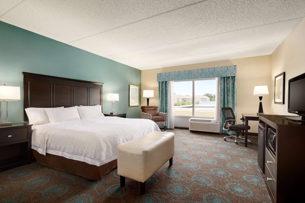 A hotel room with a large bed, a desk, a chair, and a television.