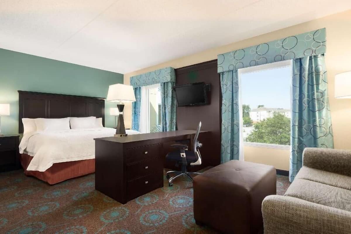 A hotel room with a bed, a desk, a chair, a TV, and a window with curtains.