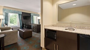 A compact hotel room with a kitchenette, a sofa, a dining table, and a large mirror. - Hampton Inn & Suites Bluffton-Sun City (Bluffton)