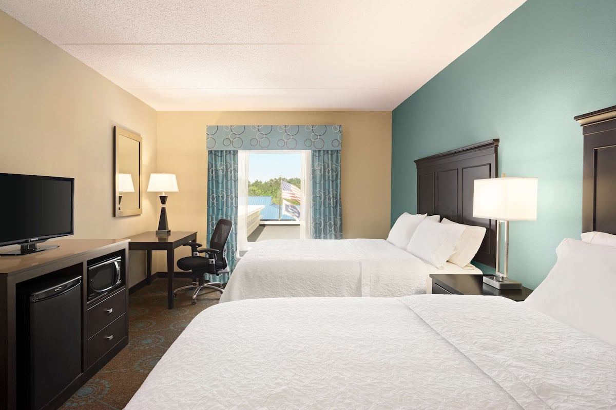 A hotel room with two beds, a desk with a chair, a television, and a window with curtains.