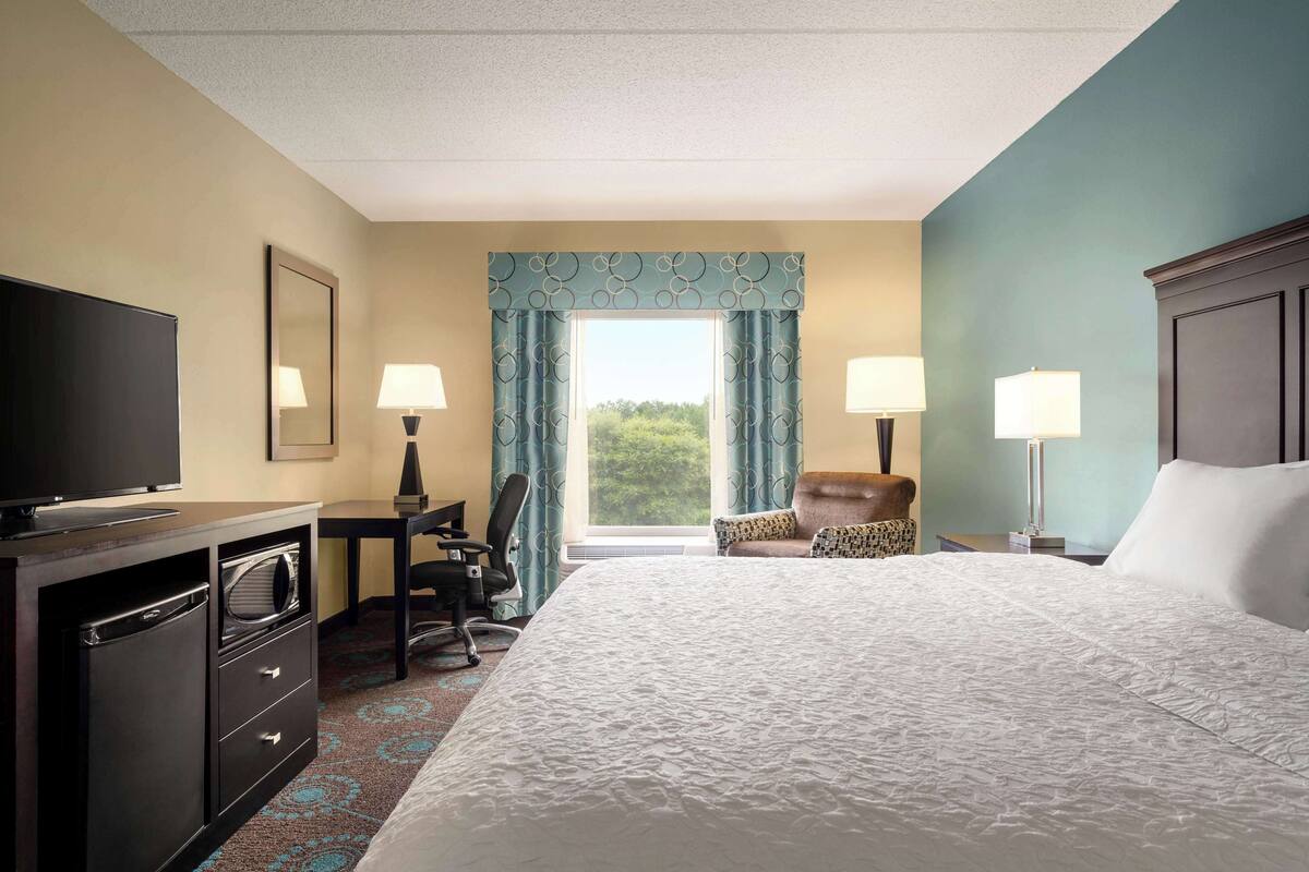 A hotel room with a large bed, a desk with a chair, a television, and two lamps.