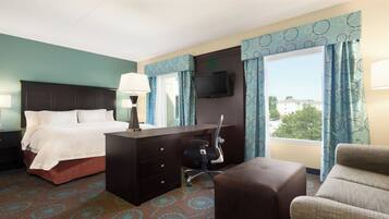 A hotel room with a bed, desk, chair, and ottoman.