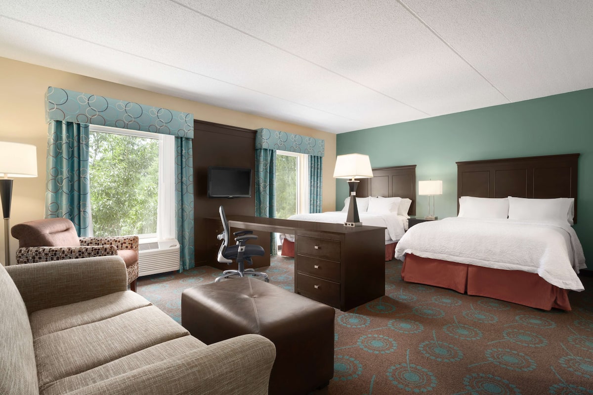 A hotel room with a bed, a desk, a chair, a sofa, and a TV.