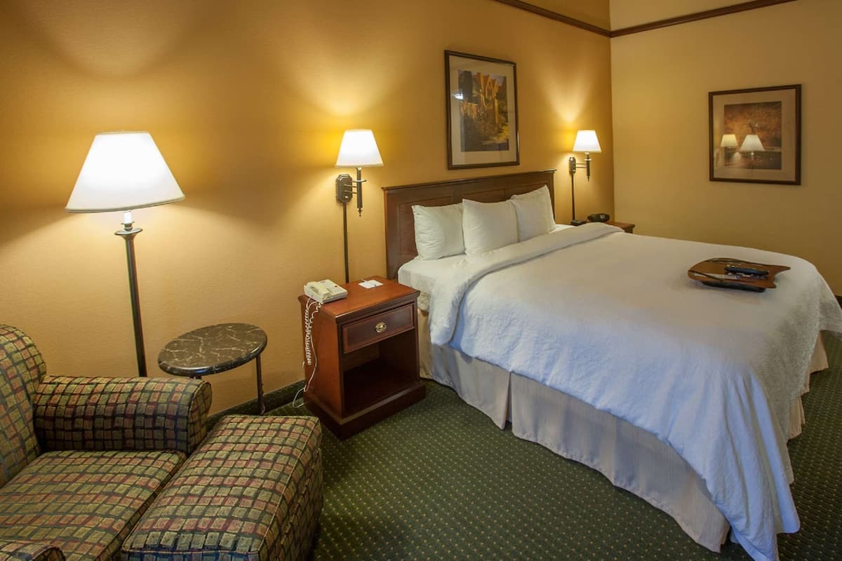 A hotel room with a bed, two bedside lamps, a nightstand with a phone, a chair, and a small table.