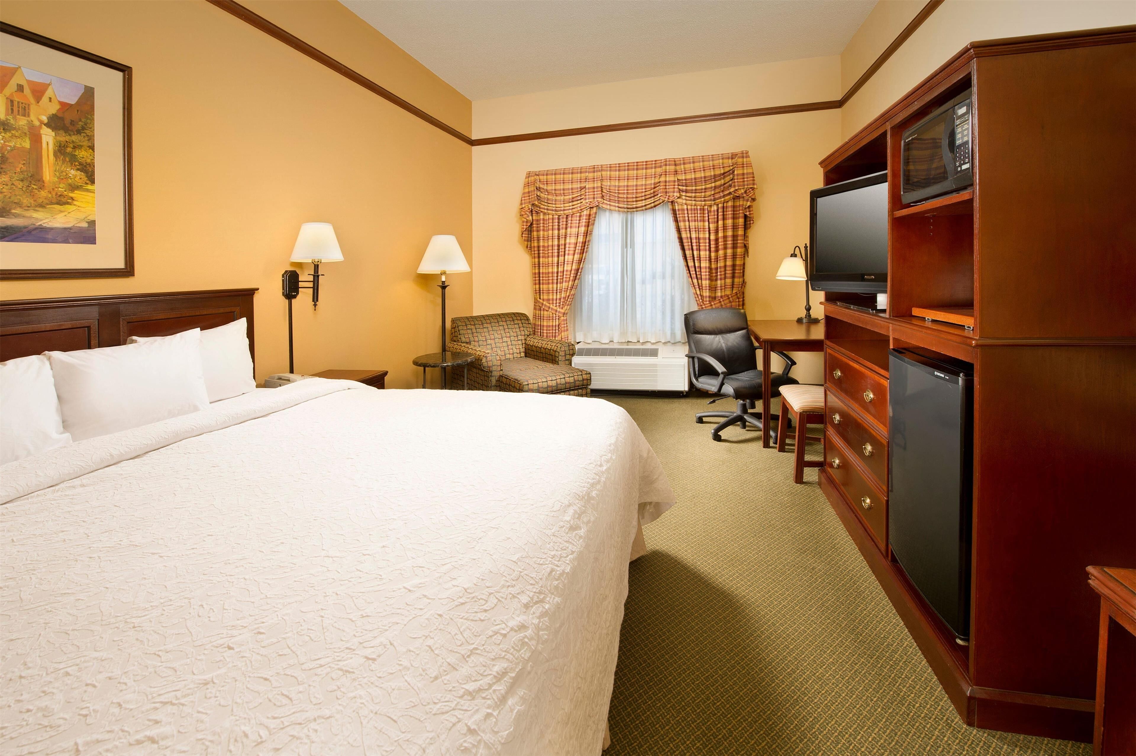 A hotel room with a large bed, a television, a desk with a chair, and a wardrobe.