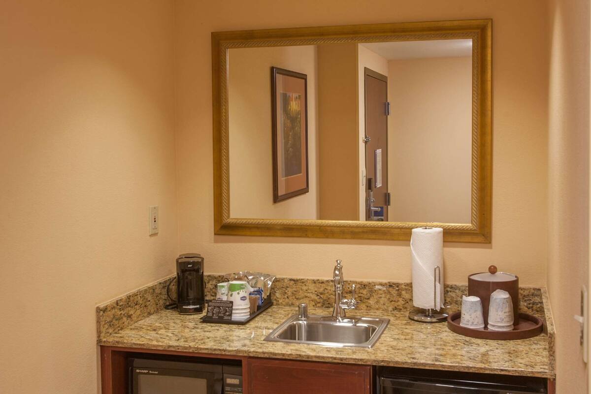 A hotel bathroom with a granite countertop, a sink, a mirror, a coffee maker, and toiletries.