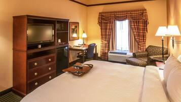 A hotel room with a large bed, a desk with a chair, a television, and a window with curtains.