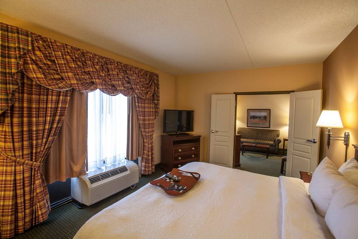A hotel room with a large bed, a television, a dresser, and a desk with a lamp.