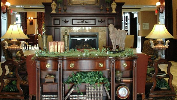 A lobby with a grand chandelier, a fireplace, and a decorative fireplace surround. There are two lamps on either side of the fireplace. - Hampton Inn & Suites Stillwater (Stillwater)