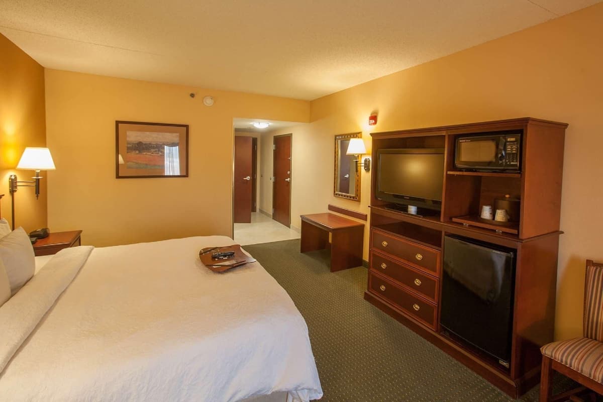 A hotel room with a bed, a desk with a TV, a microwave, and a chair.