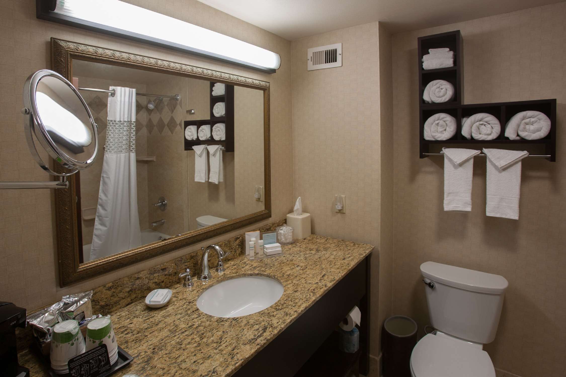 A bathroom with a granite countertop, a sink, a mirror, a toilet, and a towel rack with folded towels.