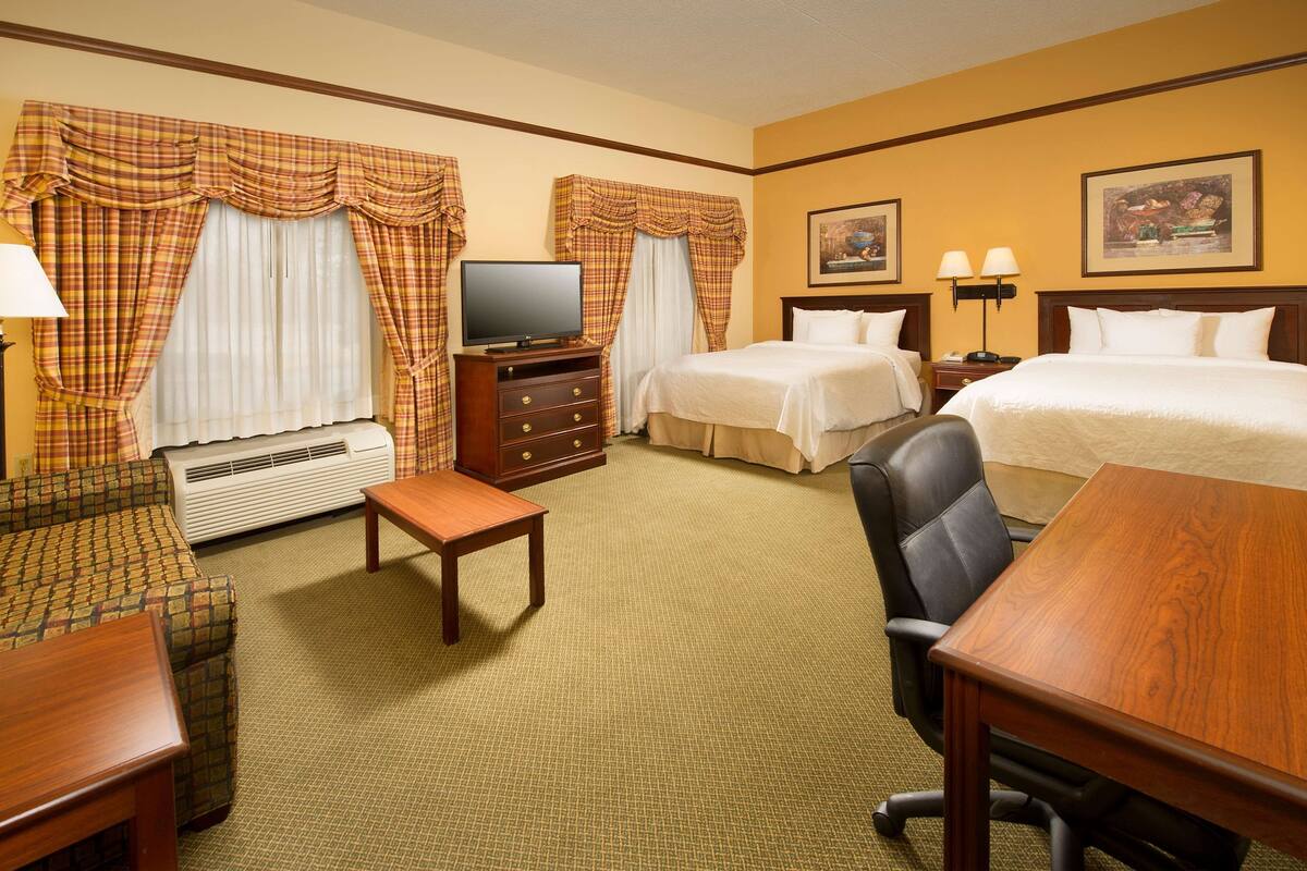 A hotel room with two beds, a TV, a desk, a chair, and a sofa.