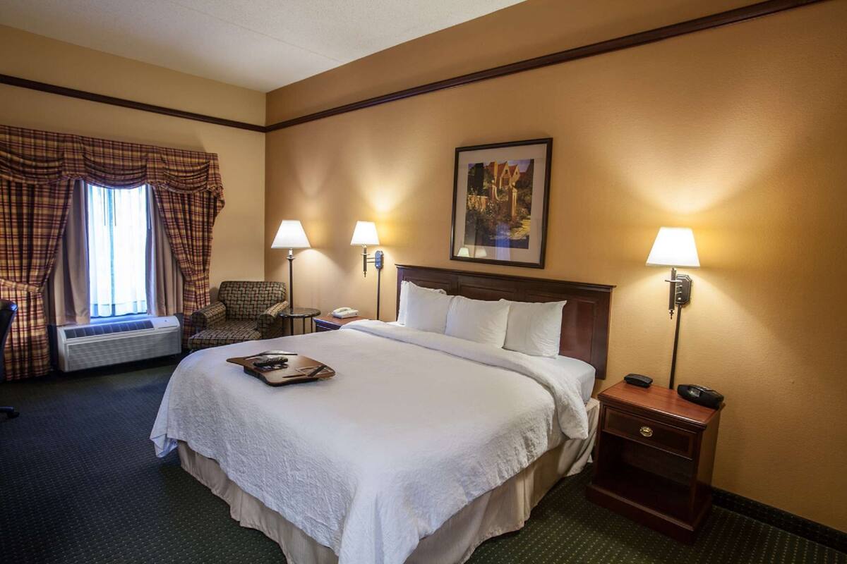 A hotel room with a large bed, two bedside lamps, a chair, a small table, and a picture on the wall.