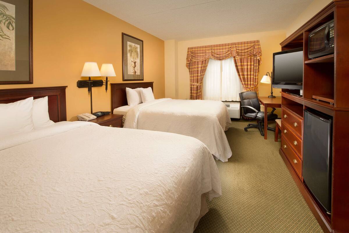 A hotel room with two beds, a desk with a television, a microwave, and a chair.