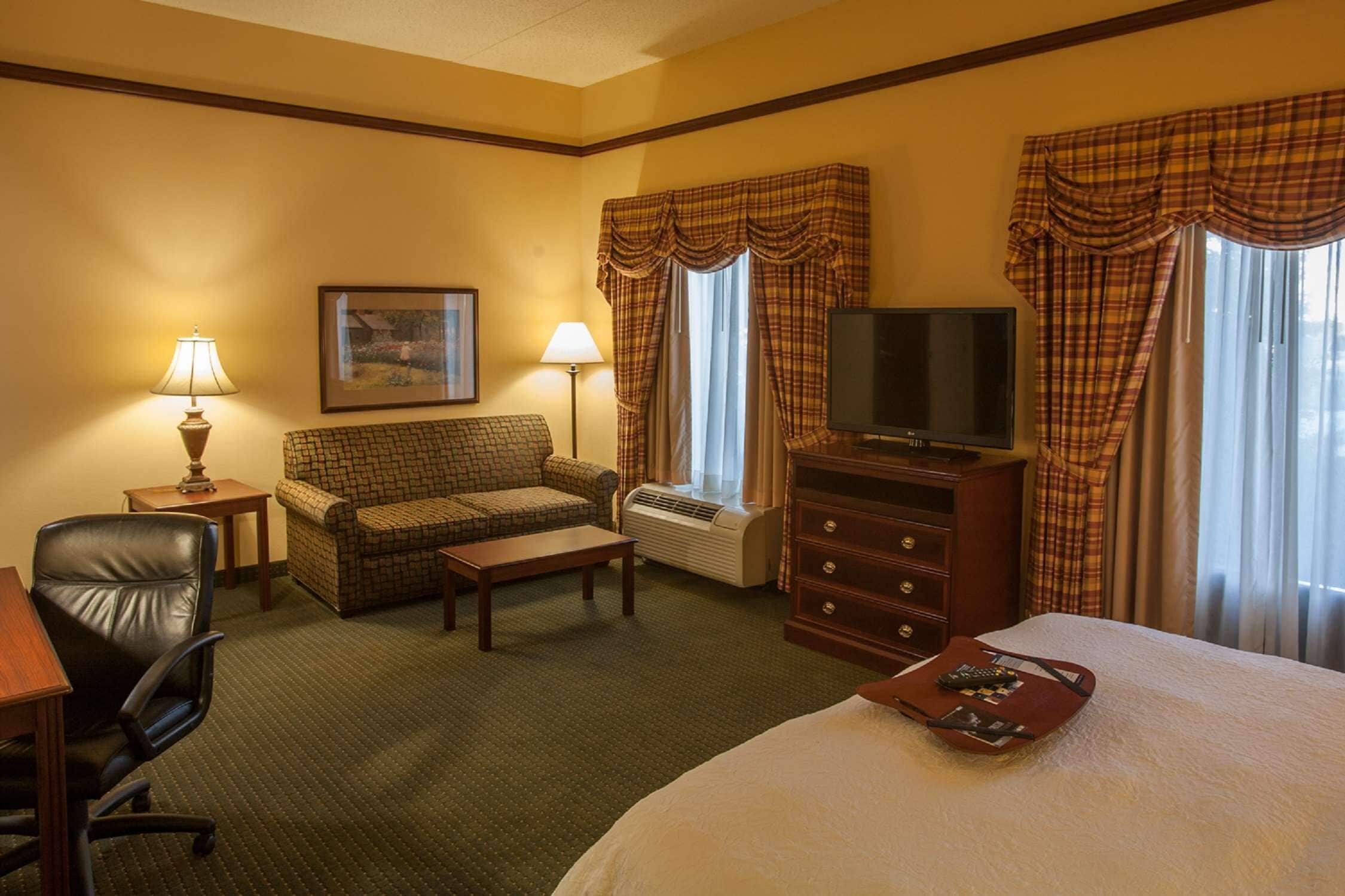 A hotel room with a bed, a TV, a desk with a chair, a sofa, a coffee table, and a dresser.