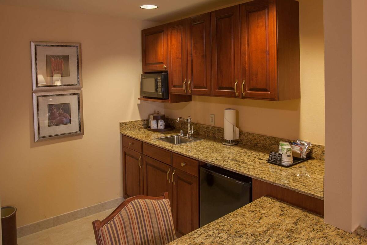 A compact kitchen with granite countertops, wooden cabinets, a microwave, a dishwasher, and a sink.