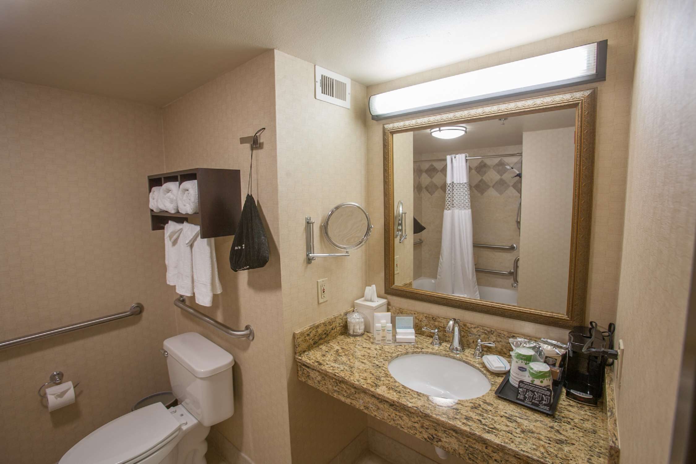 A bathroom with a toilet, sink, and mirror. There are towels and toiletries on the counter.
